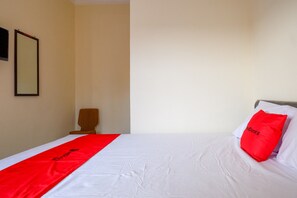 Une chambre d’hôtel avec un lit bien fait, une couvre-lit rouge et blanche, un seul oreiller rouge et une chaise placée contre le mur.