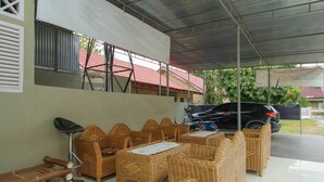 A covered outdoor seating area with wicker furniture and a bench. - RedDoorz near Watervang Lubuk Linggau 2 (Lubuklinggau)