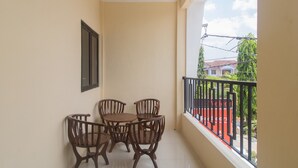 Un balcon avec une table et quatre chaises, une rambarde noire et une vue sur des immeubles et des arbres.