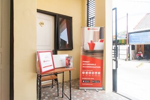 A hotel entrance with a RedDoorz sign, a framed certificate on a table, and a tiled floor.
