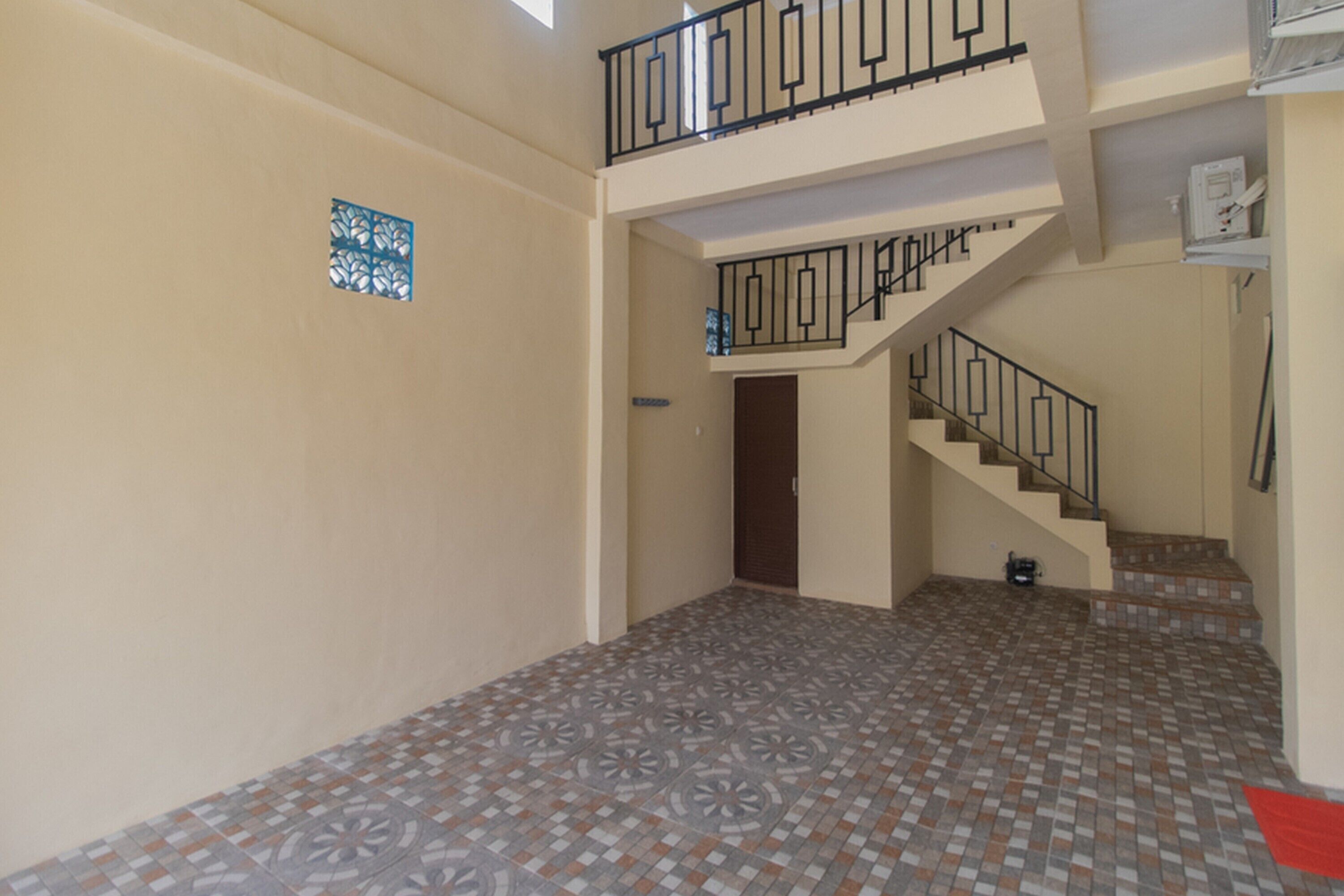 A spacious hallway with patterned floor tiles, a staircase with black railings, and a door leading to another room.
