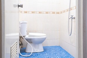 A small bathroom with a toilet, a shower, and a blue patterned floor. - RedDoorz Syariah near Grand Kota Bintang (Bekasi)