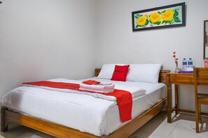 A neatly made bed with white and red bedding, a wooden headboard, and a small wooden table beside it. - RedDoorz Syariah near Grand Kota Bintang (Bekasi)