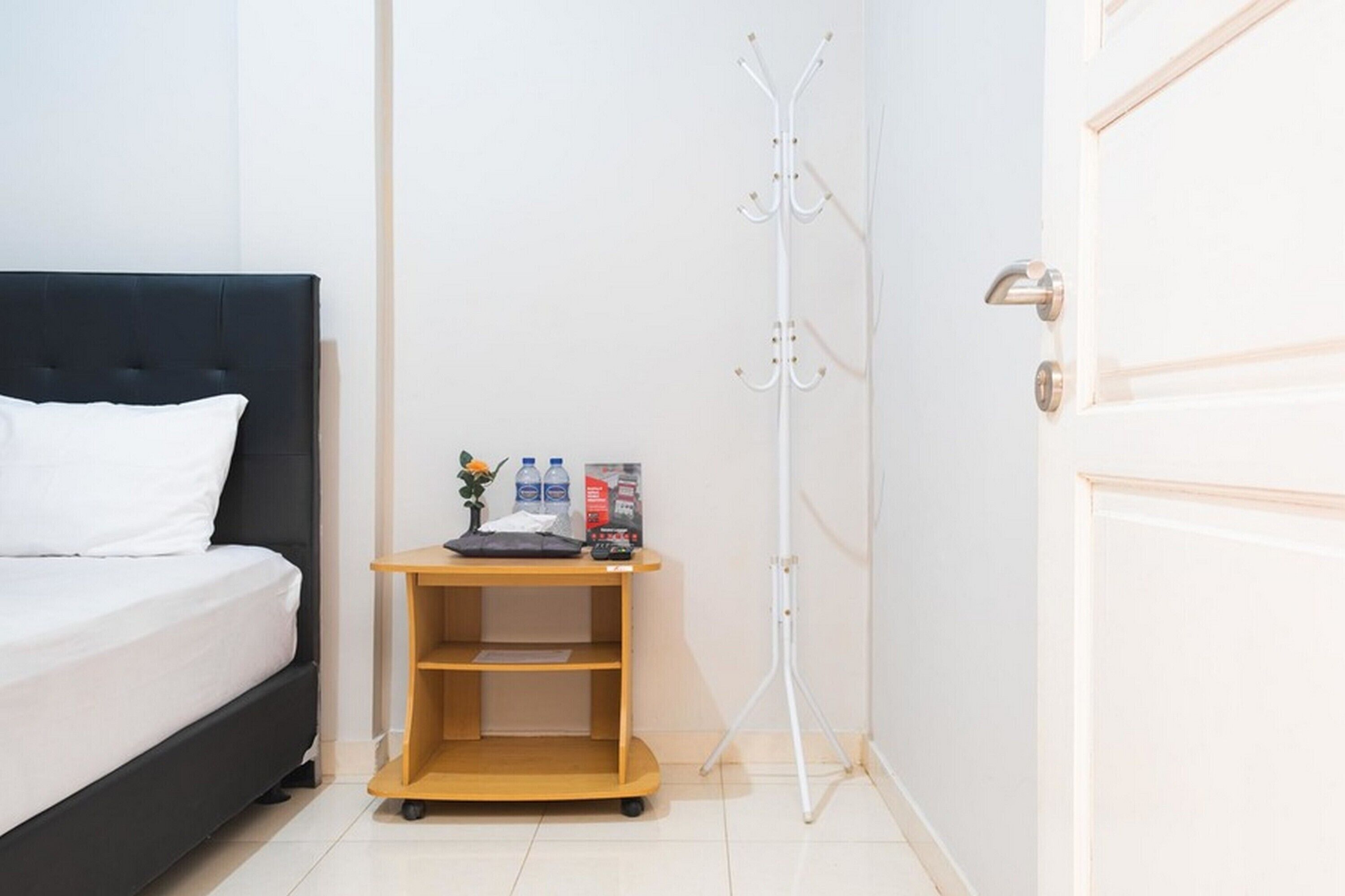 A hotel room with a bed, a wooden side table with a tray, a coat rack, and a door.