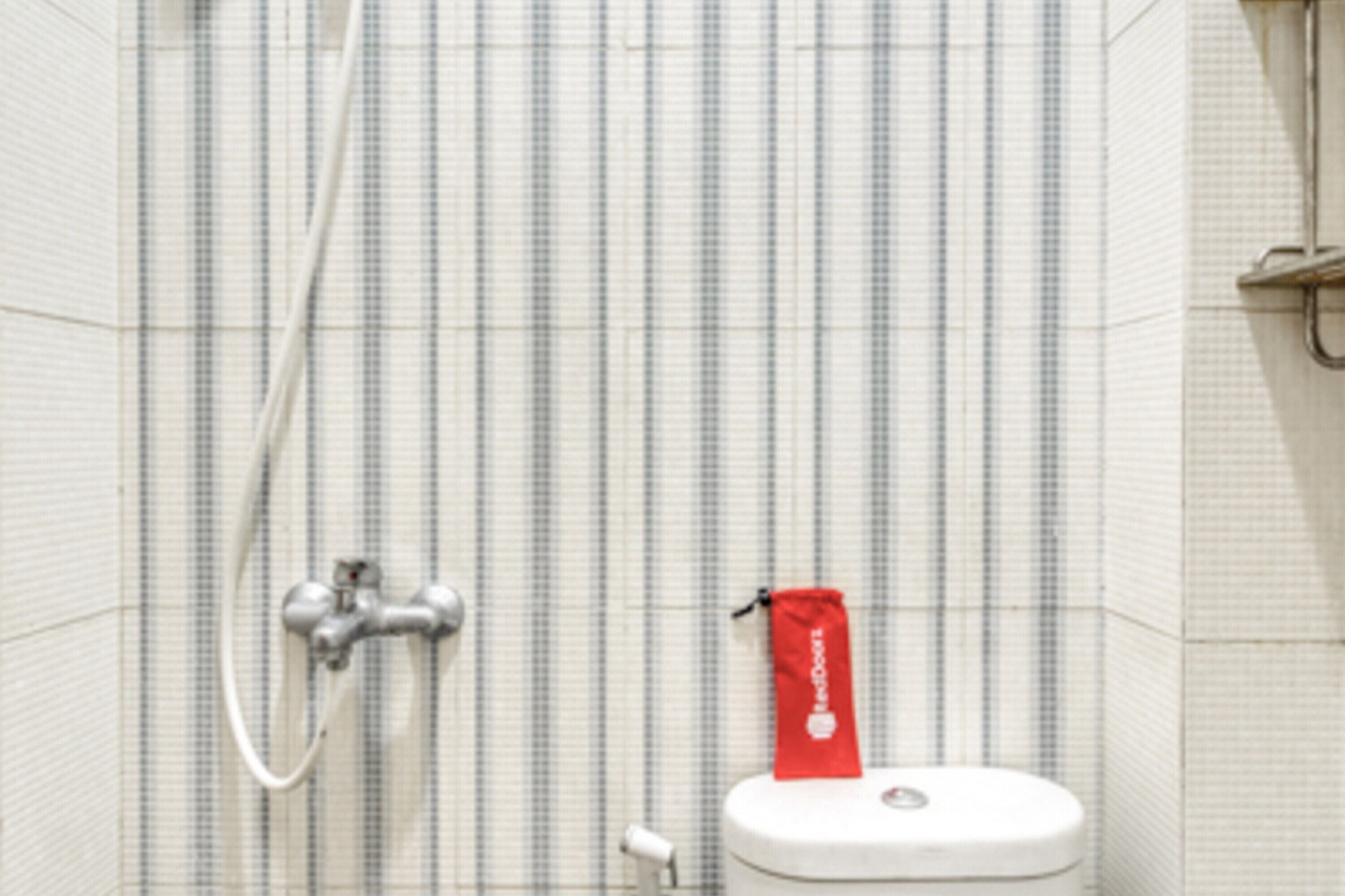 A bathroom with a striped tile wall, a white toilet, a red towel, and a shower head.