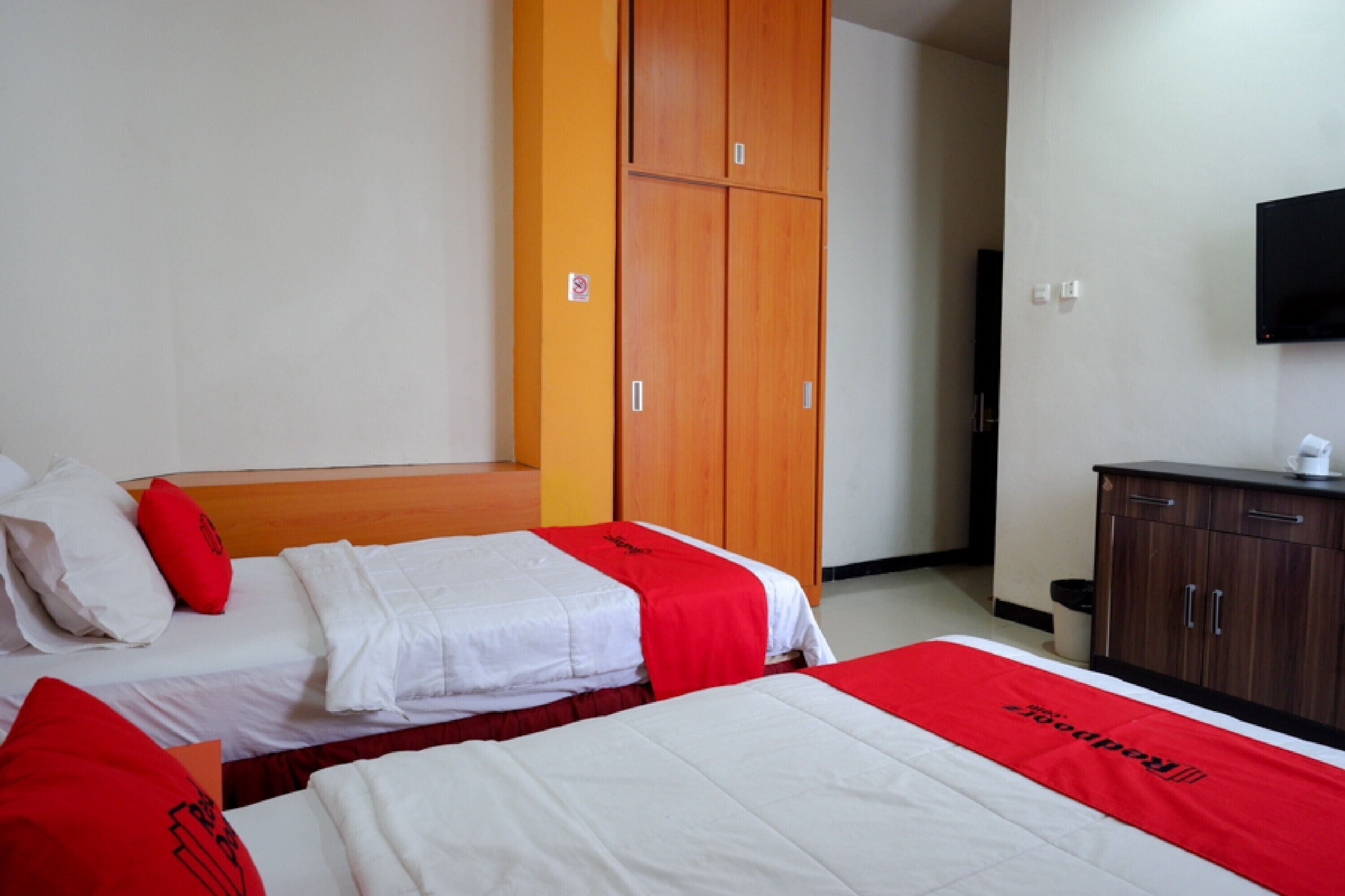 A hotel room with two beds, a wardrobe, and a television on the wall.