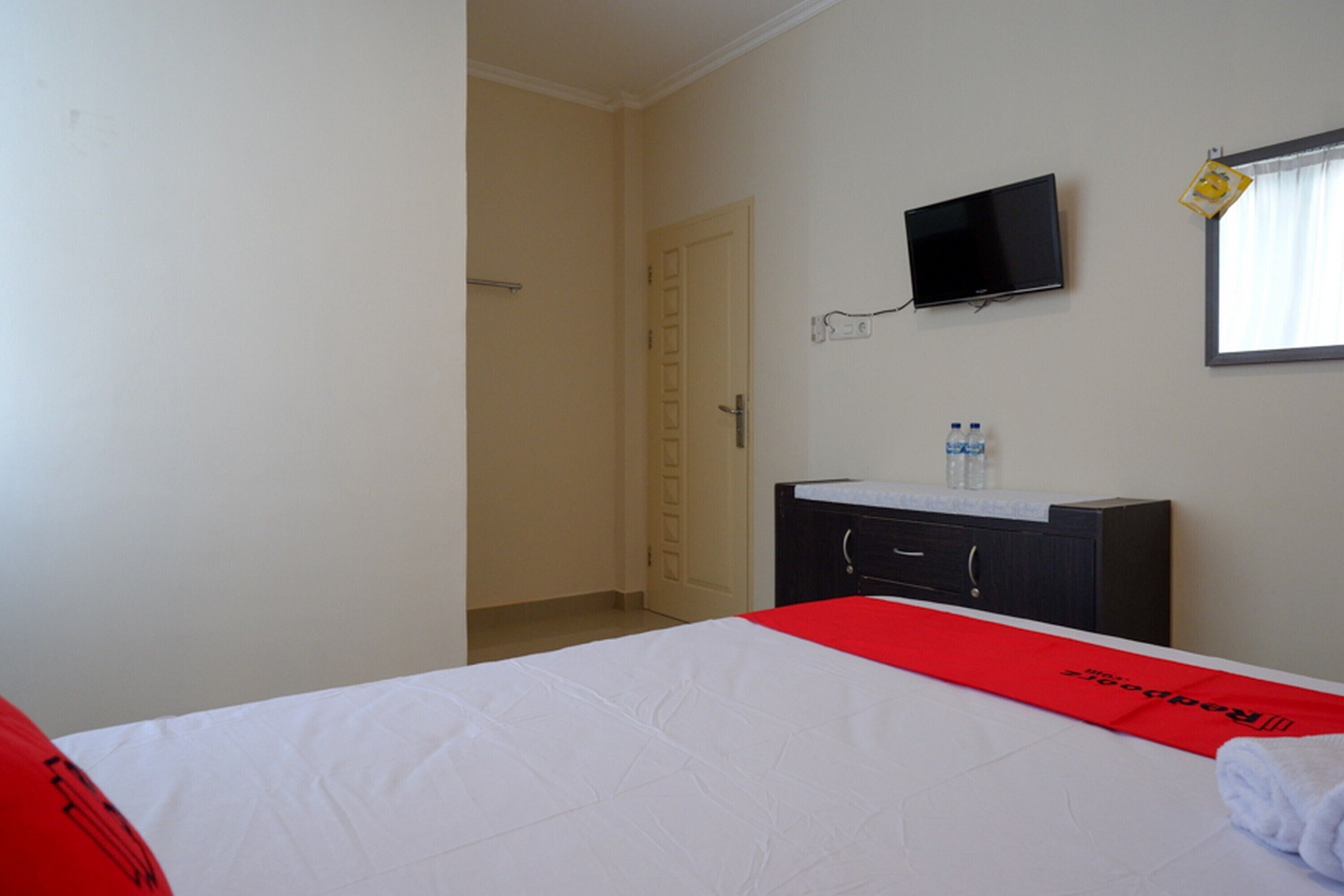 A hotel room with a bed, a TV mounted on the wall, a bathroom with a sink, and a door leading to another room.