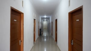 A long, narrow hallway with wooden doors on both sides, leading to a bright room at the end. - RedDoorz near Pasar Baru Mamuju (Mamuju)