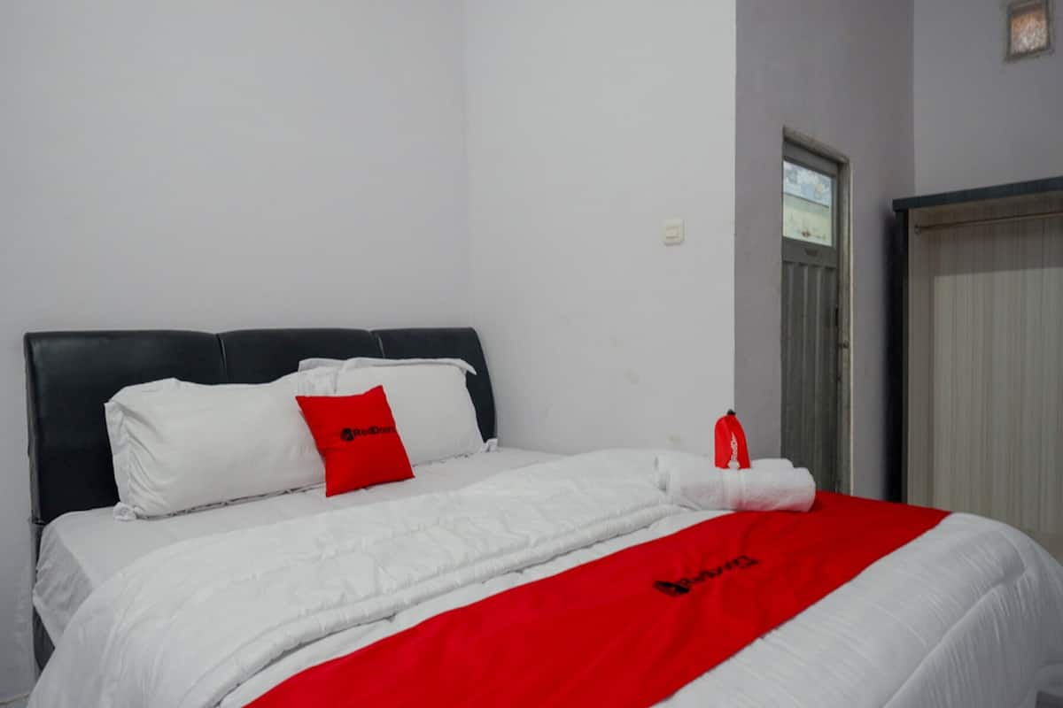 A hotel room with a bed, white bedding, a red throw blanket, and a red pillow.