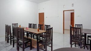 A dining area with a wooden table and chairs, white walls, and a tiled floor. - RedDoorz near Pasar Baru Mamuju (Mamuju)
