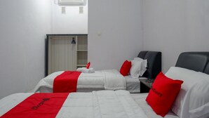 A hotel room with two beds, each with white bedding and red accents, a small table, and a wardrobe. - RedDoorz near Pasar Baru Mamuju (Mamuju)