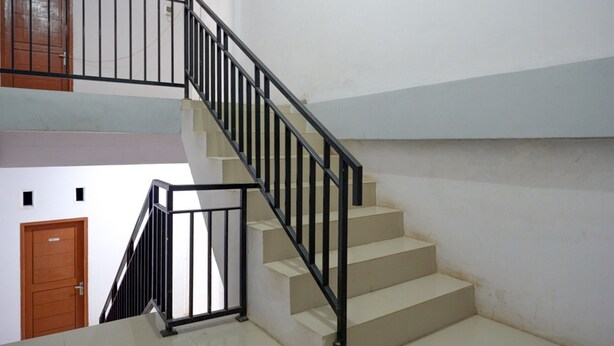 A staircase with a black metal railing and beige steps, leading to an upper floor. - RedDoorz near Pasar Baru Mamuju (Mamuju)