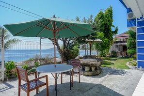 Une terrasse avec une table ronde et des chaises, un parasol vert et une vue sur la mer.
