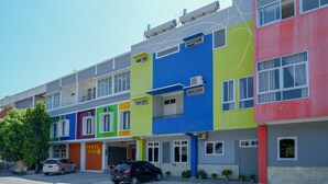 A row of colorful residential buildings with multiple floors, air conditioning units, and a paved street with parked cars. - RedDoorz Plus Syariah @ Hotel Boulevard Luwuk (Luwuk)