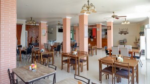 A spacious dining area with brick pillars, multiple tables and chairs, ceiling fans, and a bright interior. - RedDoorz Plus Syariah @ Hotel Boulevard Luwuk (Luwuk)
