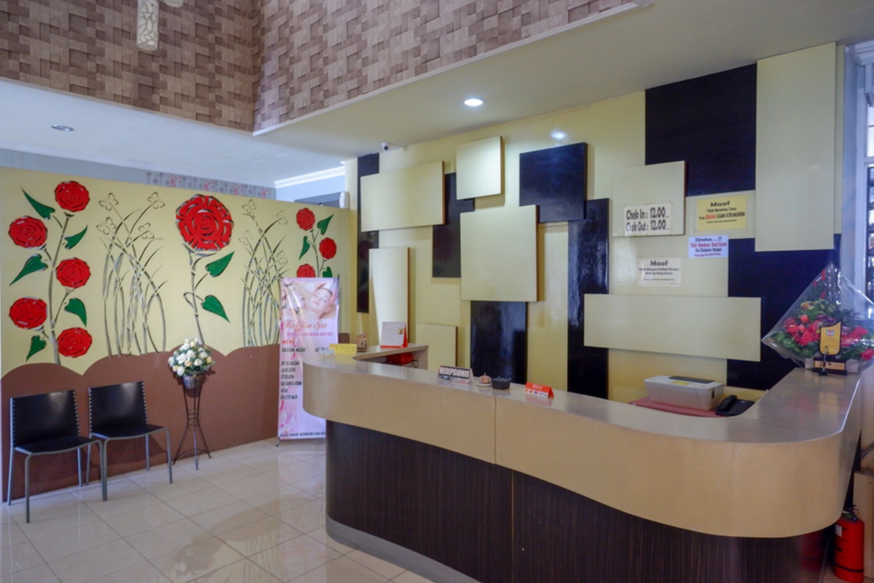 A hotel reception area with a reception desk, two chairs, a wall with floral artwork, and a fire extinguisher.