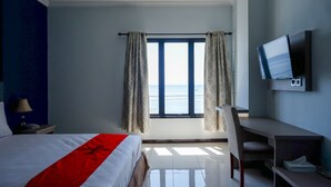 A hotel room with a bed, a desk, a chair, a TV, and a window with curtains. - RedDoorz Plus Syariah @ Hotel Boulevard Luwuk (Luwuk)