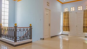 A spacious hallway with a polished floor, a staircase with a decorative railing, and a door with a small window. - RedDoorz Syariah @ Puri Kalijaga Street (Cirebon)