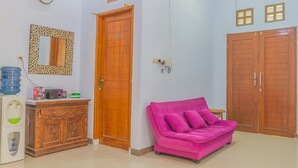 A room with a wooden door, a pink sofa, a wooden cabinet, a mirror, and a clock on the wall. - RedDoorz Syariah @ Puri Kalijaga Street (Cirebon)