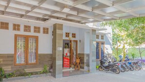 A building with a covered entrance, a wooden door, and a row of parked motorcycles outside. - RedDoorz Syariah @ Puri Kalijaga Street (Cirebon)