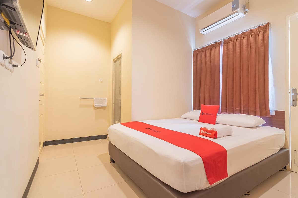 Een hotelkamer met een bed, een rode spreideken, een kussen en een raam met gordijnen.