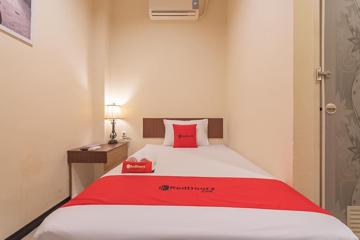 Een hotelkamer met een bed, nachtkastje, lamp en een deur met bloemenmotief.
