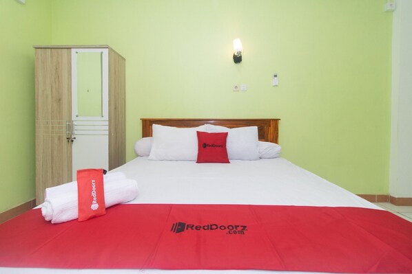 A hotel room with a bed, a red blanket, and a RedDoorz towel.