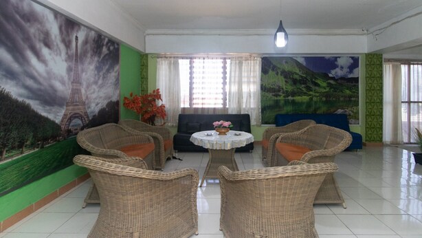 A room with wicker furniture, a round table with a vase, a sofa, and a large mural of the Eiffel Tower. - RedDoorz @ Frans Seda Kupang (Kupang)