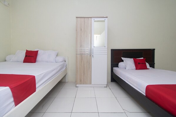 Une chambre d’hôtel avec deux lits, chacun agrémenté d’un oreiller rouge et d’une couvre-lit blanche. La chambre est équipée d’une armoire avec un miroir et une porte, et le sol est recouvert de carreaux blancs.