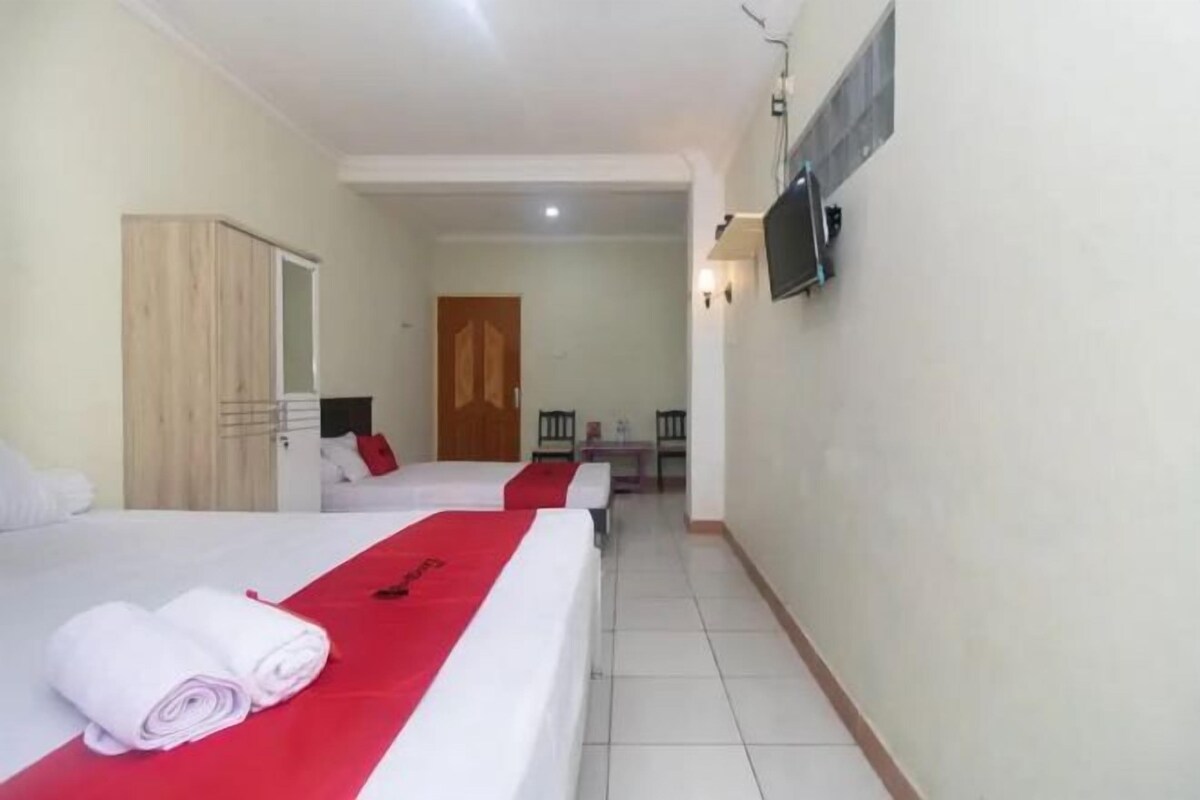 A hotel room with two beds, a wooden wardrobe, a TV mounted on the wall, and a door leading to another room.