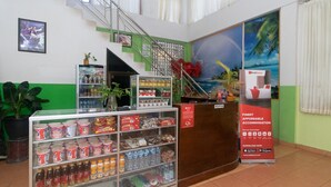 A reception area with a counter, a refrigerator stocked with beverages, and a staircase leading to an upper level. - RedDoorz @ Frans Seda Kupang (Kupang)
