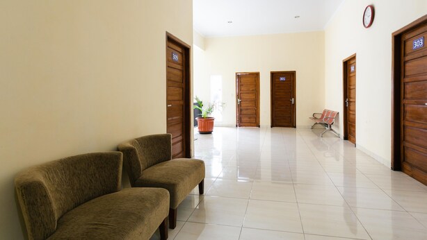 A hallway with two brown sofas, wooden doors numbered 303 and 901, and a potted plant. - RedDoorz Syariah near Purwosari Train Station (Surakarta)