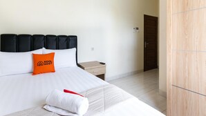 A hotel room with a bed, a nightstand, a wooden wardrobe, and a door. - RedDoorz Syariah near Purwosari Train Station (Surakarta)