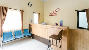 A reception area with a wooden counter, blue seating, a clock, and a sign reading "SOLOA guesthouse". - RedDoorz Syariah near Purwosari Train Station (Surakarta)