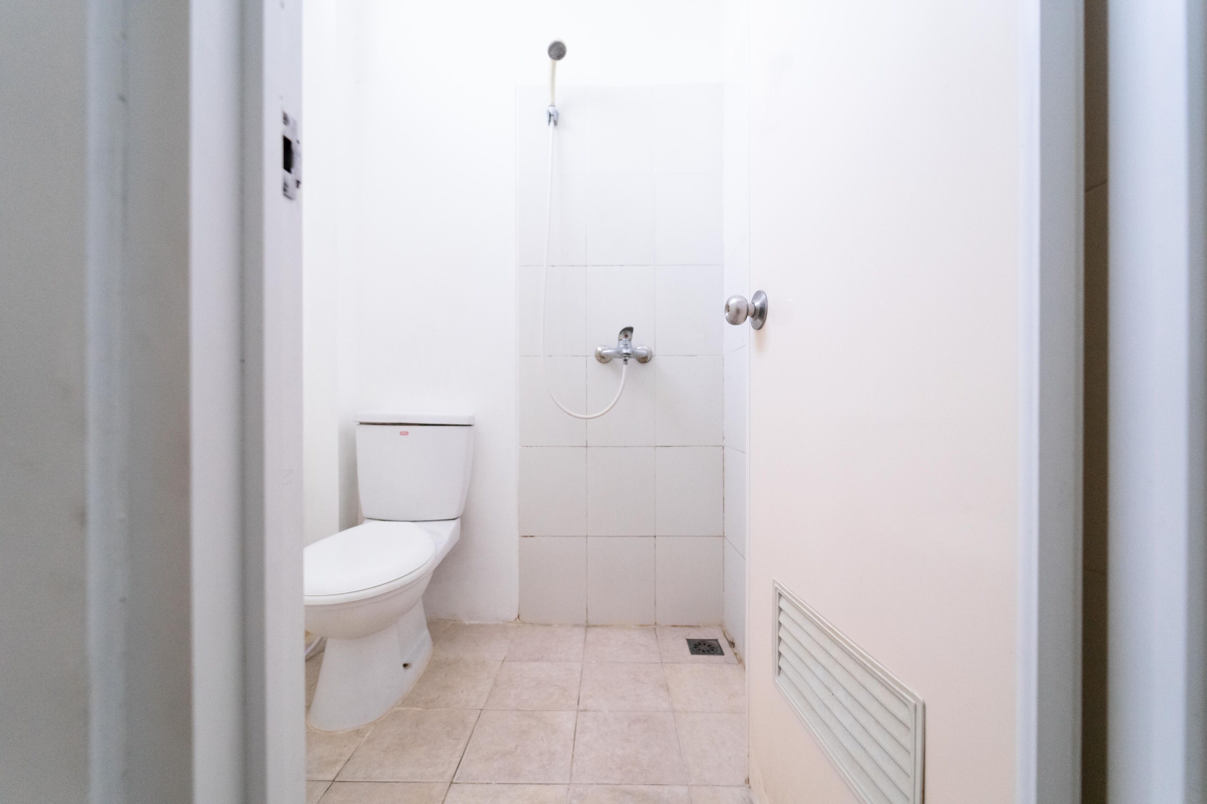 A small, white bathroom with a toilet, a shower, and a vent on the wall.