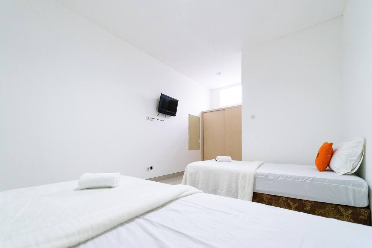 A hotel room with two beds, a TV mounted on the wall, and a wooden door.