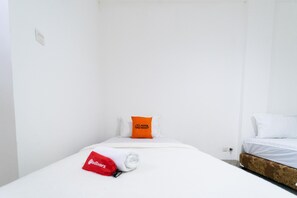 Ein kleines, sauberes Zimmer mit einem Bett, einem roten Handtuch und einem Kopfkissen mit einem Logo.