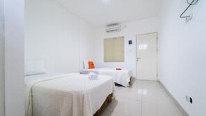 A hotel room with two beds, a white tiled floor, a door, and an air conditioning unit on the wall.