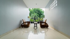 A room with a tiled floor, two wicker chairs, a small table, and a view of greenery through a window.