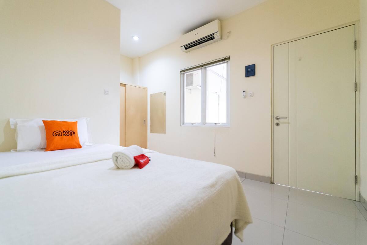 A hotel room with a bed, a window, an air conditioning unit, and a door.