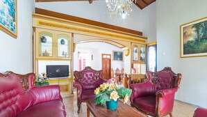 A spacious living room with red leather sofas, a wooden coffee table with flowers, and a television. - RedDoorz Syariah near Balai Kota Batu (Batu)