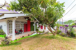 Una casa con porche, puerta roja y un árbol en el jardín.