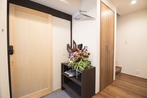 A hallway with wooden flooring, a shoe rack, and a floral arrangement on a shelf. - Kyoto Nakamuraya Enmachi Bettei (Kyoto)