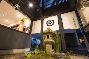 Traditional Japanese building with a stone lantern and bamboo surroundings, featuring a car parked outside.
