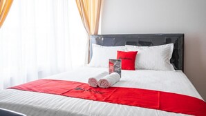 Una habitación de hotel con una cama bien hecha, ropa de cama blanca y detalles en rojo, además de una toalla roja.