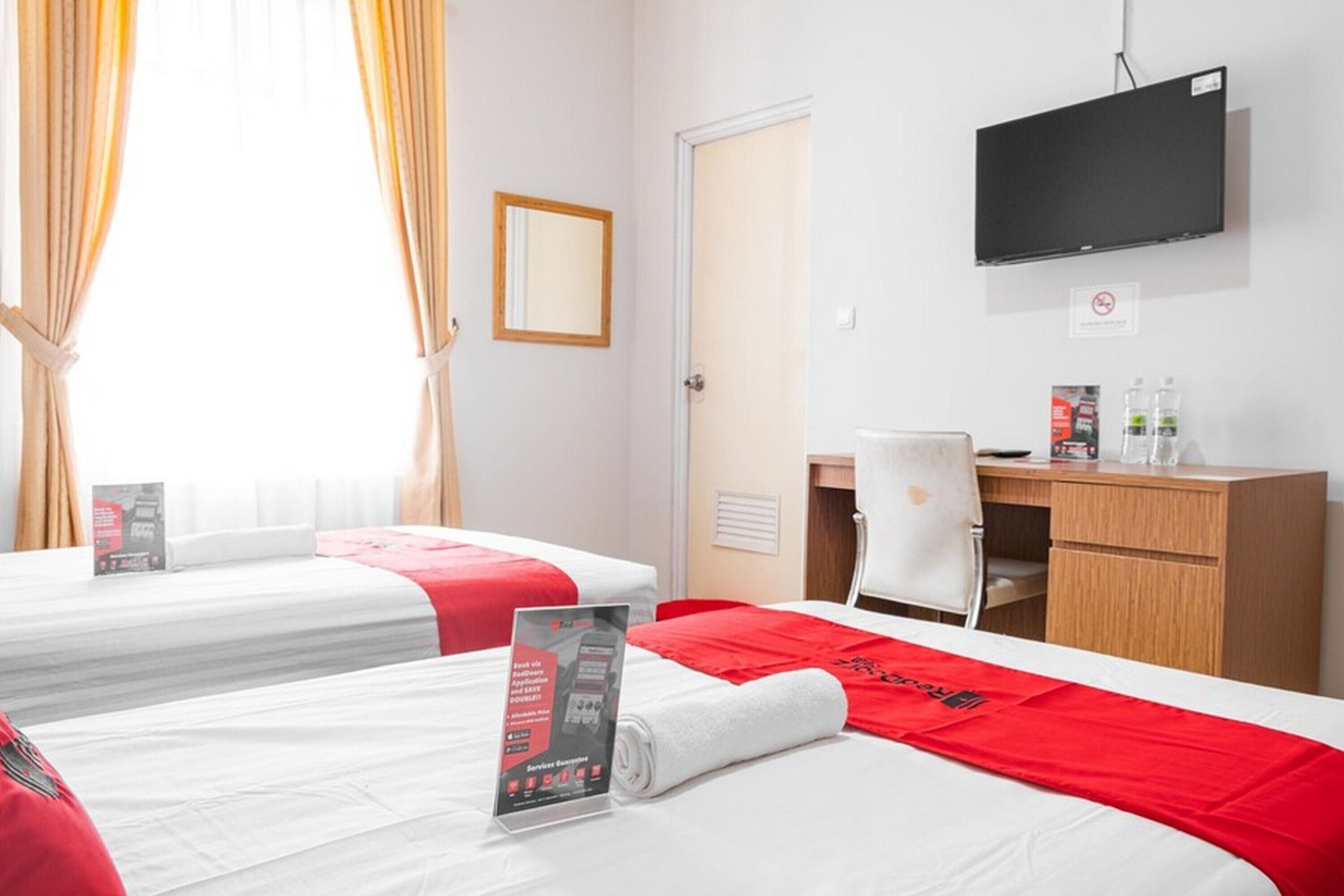 Hotellihuone, jossa on kaksi sänkyä, työpöytä, tuoli, televisio ja ikkuna, jossa on verhot.