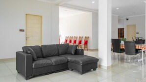 Una sala de estar moderna con un sofá seccional, un comedor con mesa y sillas, y una cocina al fondo.