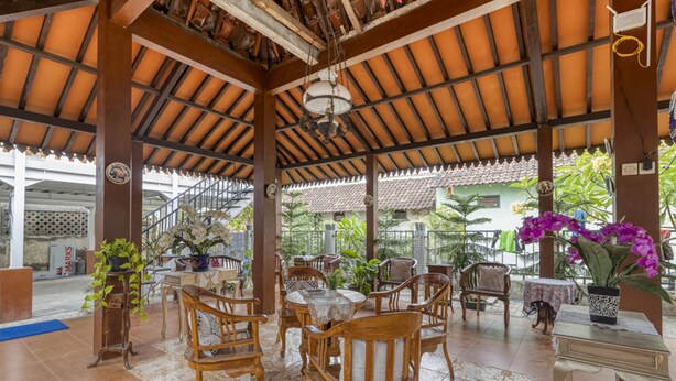 A covered outdoor seating area with wooden chairs and tables, surrounded by potted plants and a view of the street. - RedDoorz Syariah Near Wijilan 2 Yogyakarta (Yogyakarta)