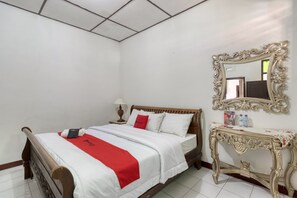 Une chambre d’hôtel avec un lit en bois, du linge de lit blanc, un plaid rouge, une table de chevet avec un miroir et une petite console avec des articles de toilette.
