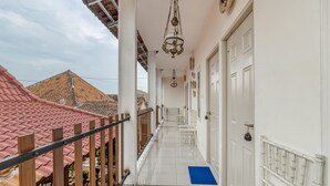 A corridor with white walls, a blue mat at the entrance, and a red-tiled roof visible in the background. - RedDoorz Syariah Near Wijilan 2 Yogyakarta (Yogyakarta)